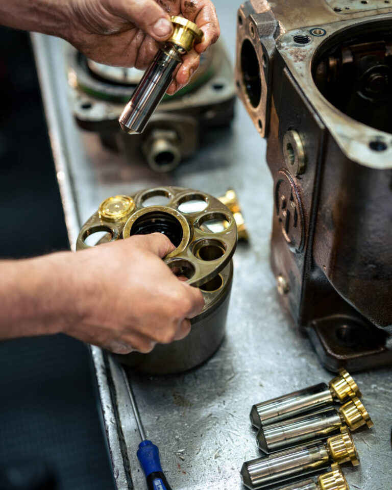 Nahaufnahme einer Hydraulikkomponente, die von einem HK Mitarbeiter geprüft wird