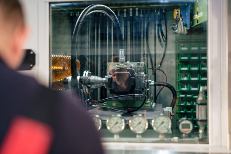 Eine Hydraulik-Komponente in einem Pruefstand hinter einer Glasscheibe
