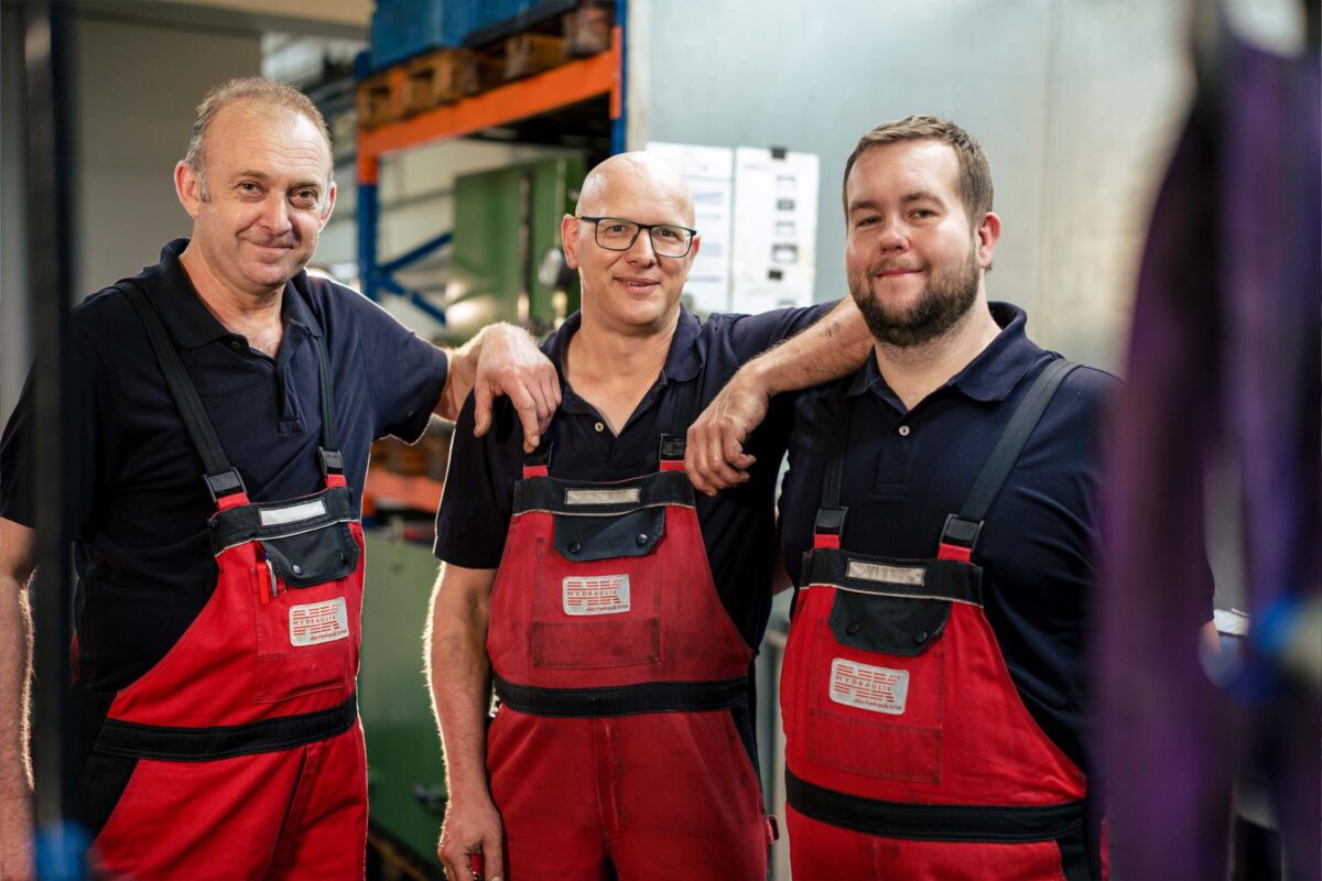 Drei HK Hydraulik Mitarbeiter stehen in der Werkstatt zusammen
